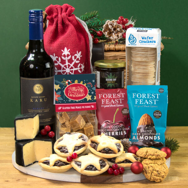 A festive hamper featuring a bottle of red or white wine, cheese, Gluten Free Crackers, cookies, a red snowflake bag, chocolate dipped almonds & cherries, chutney, and mince pies—beautifully arranged on a decorated wooden board.