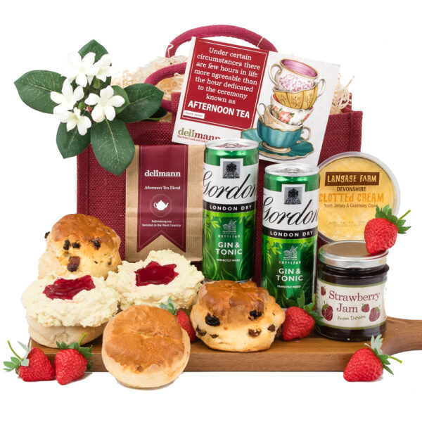 Devon Cream Tea With Gin & Tonic: A hamper featuring scones, clotted cream, strawberry jam, afternoon tea blend, strawberries, two gin & tonic cans, and a card—presented on a wooden board with floral accents.