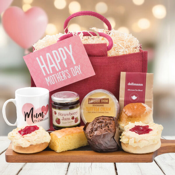 The Mum's Cream Tea Delights gift set includes a pink bag with a heartfelt card, mug, strawberry jam, clotted cream, scones, muffin, cake slice, and tea packet arranged on a wooden board. Ideal for Mother's Day!.