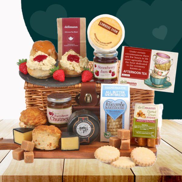 The Afternoon Tea With Cheese & Chutney Hamper sits on a wooden table, overflowing with scones, clotted cream, strawberry jam, fudge, shortbread, cheese, chutney, and afternoon tea postcard.