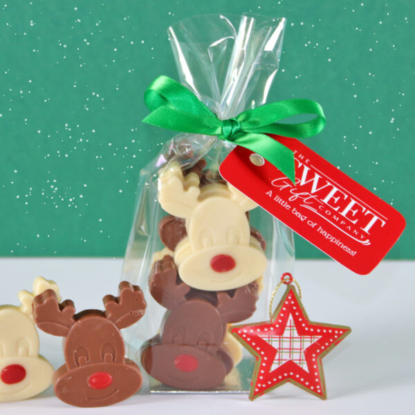 A clear bag filled with **Mini Rudolph Chocolate Reindeer**, tied with a green ribbon and a red tag, sits next to a red star ornament against a green background with white speckles.