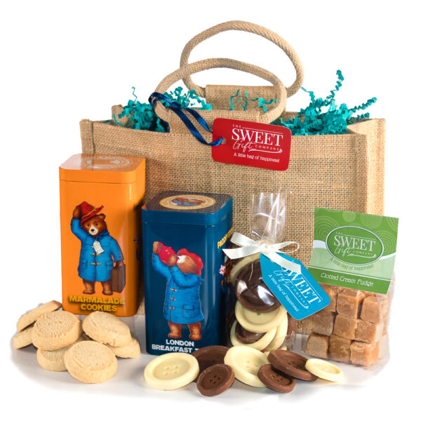 Paddington's Tea Time Treats: A charming gift bag that includes marmalade cookies, London breakfast tea, fudge, chocolate buttons, and a delightful Paddington Bear tin, all beautifully arranged with blue shredded paper.