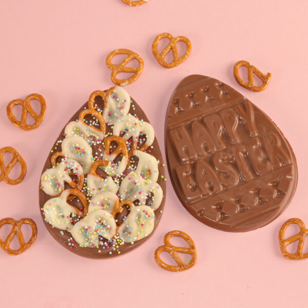 A flat chocolate Easter egg named adorned with whit chocolate covered pretzels and sprinkles, and the back embossed with "Happy Easter,".