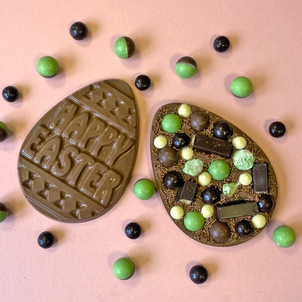 The pink background captures Easter's essence with two chocolate eggs. One features "Happy Easter," while the Marvellous Minty Easter Egg Slab is adorned with mint green and brown candies. Scattered around are vibrant candies, creating a delightful scene.