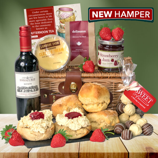 The Devon Cream Tea With Champagne Truffles & Wine hamper features wine, cheese, scones with cream and jam, strawberry jam, chocolates, tea, and fresh strawberries in a wicker basket.